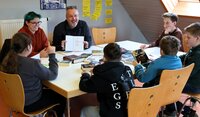 Autorin Alina Hesse und Jugendpfleger Kai Faßnacht sitzen mit Jugendlichen um einen Tisch. In der Mitte liegen viele Bücher.